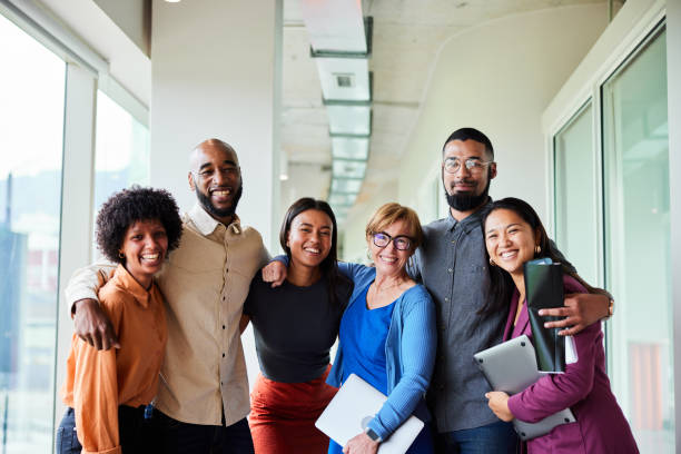 joie au travail Portrait of a group of diverse businesspeople smiling while standing arm in arm together in an office corridor